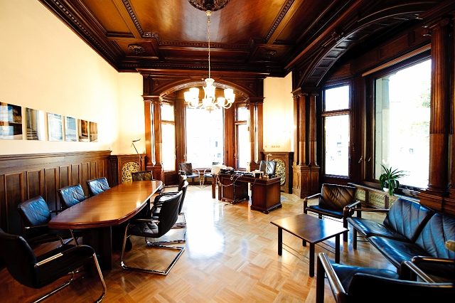 Holzgetäfelter Raum mit großen Fenstern, ovalem Tisch und Ledersesseln