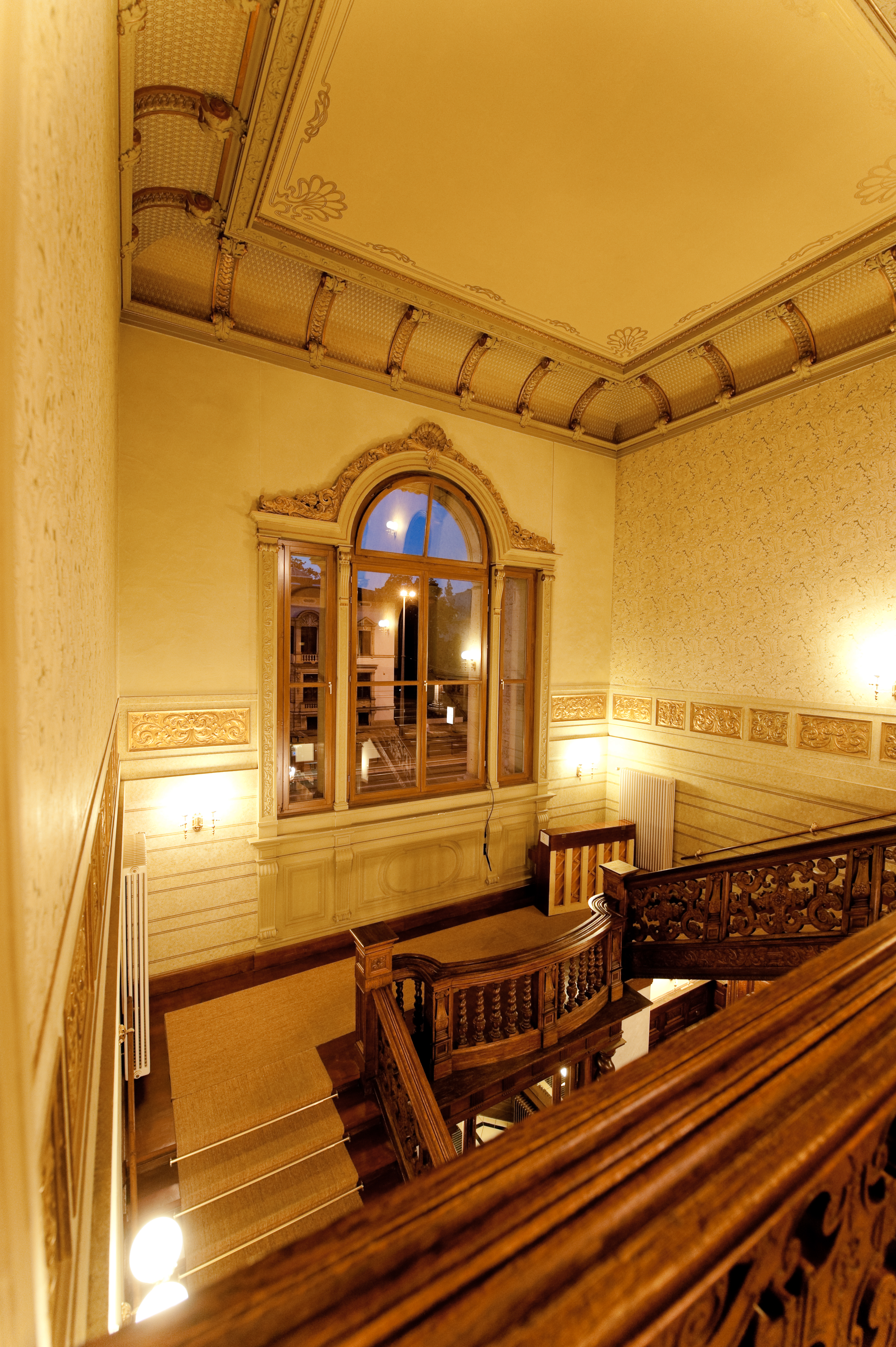 Treppenaufgang aus Holz im inneren einer historischen Villa, im Hintergrund ist ein großes Fenster zu sehen
