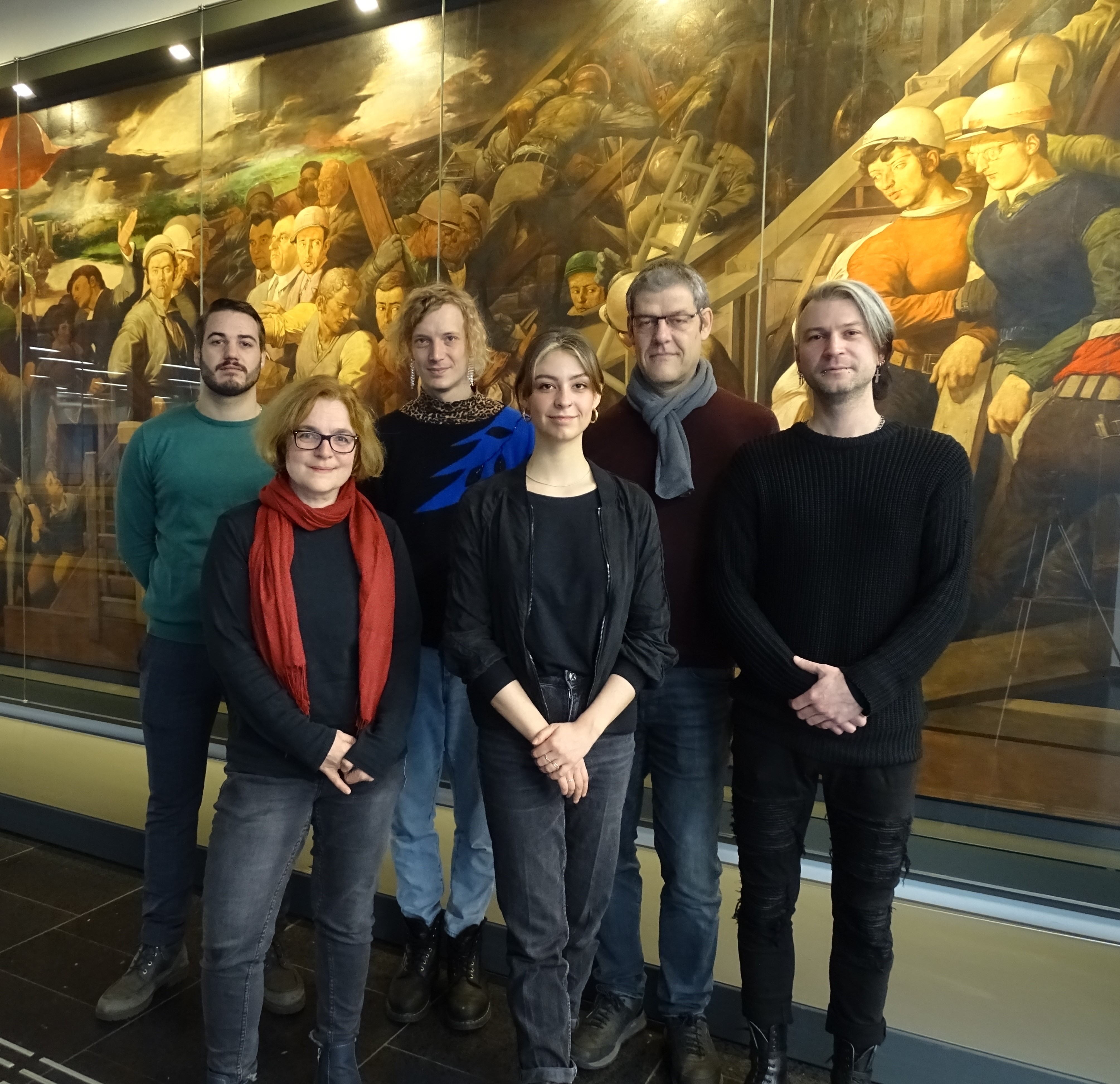 Sechs Personen stehen vor einem Gemälde und schauen in die Kamera