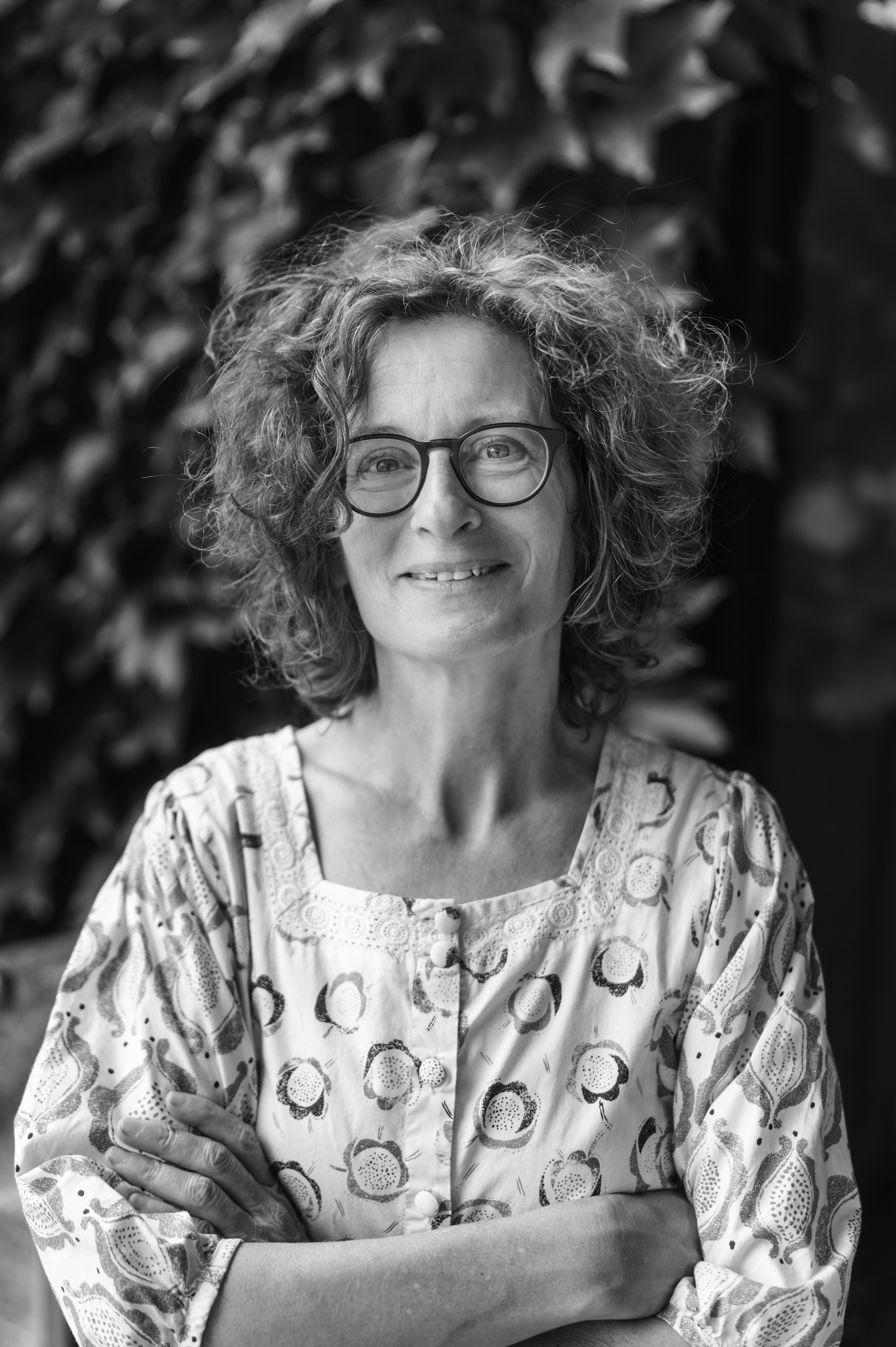 Black-and-white portrait photograph of a woman wearing glasses in front of plants