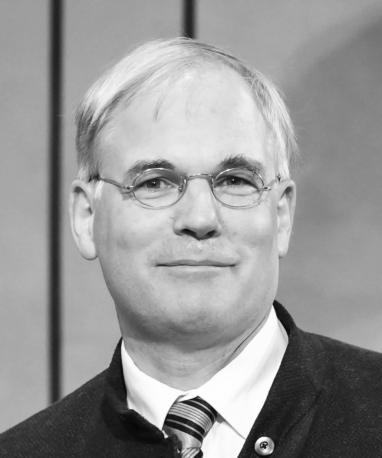 Black-and-white portrait photograph of a smiling man wearing glasses and a suit