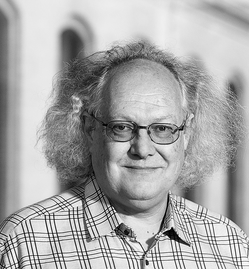 Black-and-white portrait photograph of a smiling man wearing glasses and a checked shirt