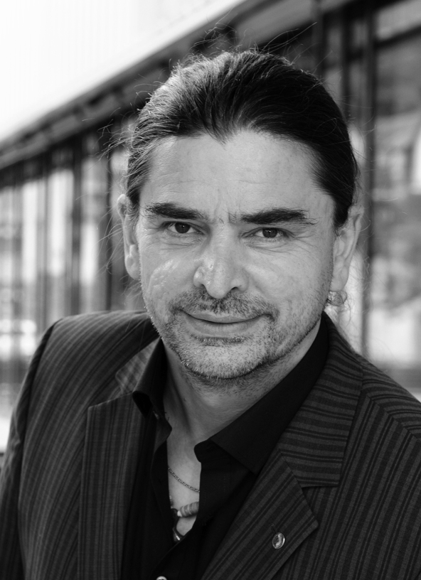 Black-and-white portrait photograph of a smiling man in front of a glass façade